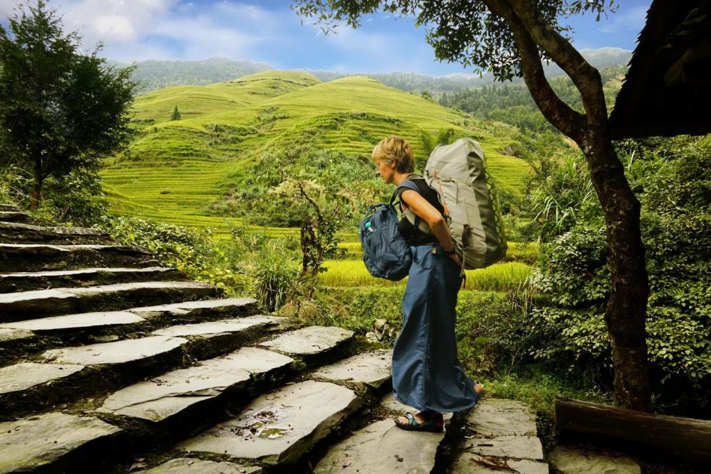 a woman with a backpack standing on some rocks at Longji Terrace La vie Inn in Longsheng