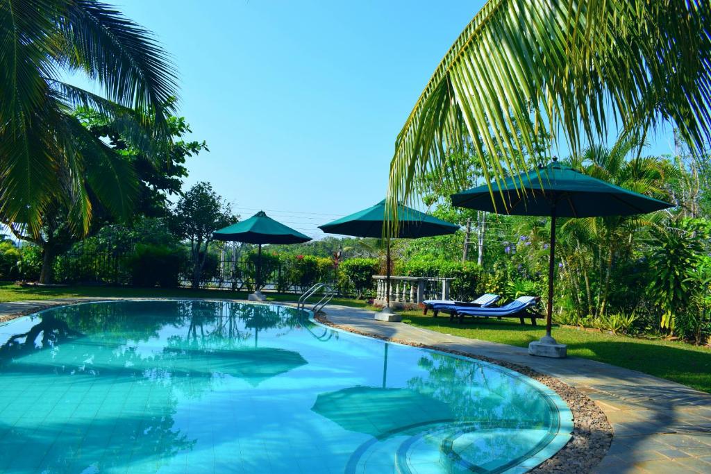 a swimming pool with two umbrellas and a bench at Asian Jewel Boutique Hotel in Hikkaduwa