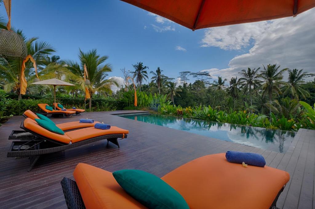 een zwembad met oranje ligstoelen en een resort bij Villa Tegal Tis Ubud - CHSE Certified in Payangan