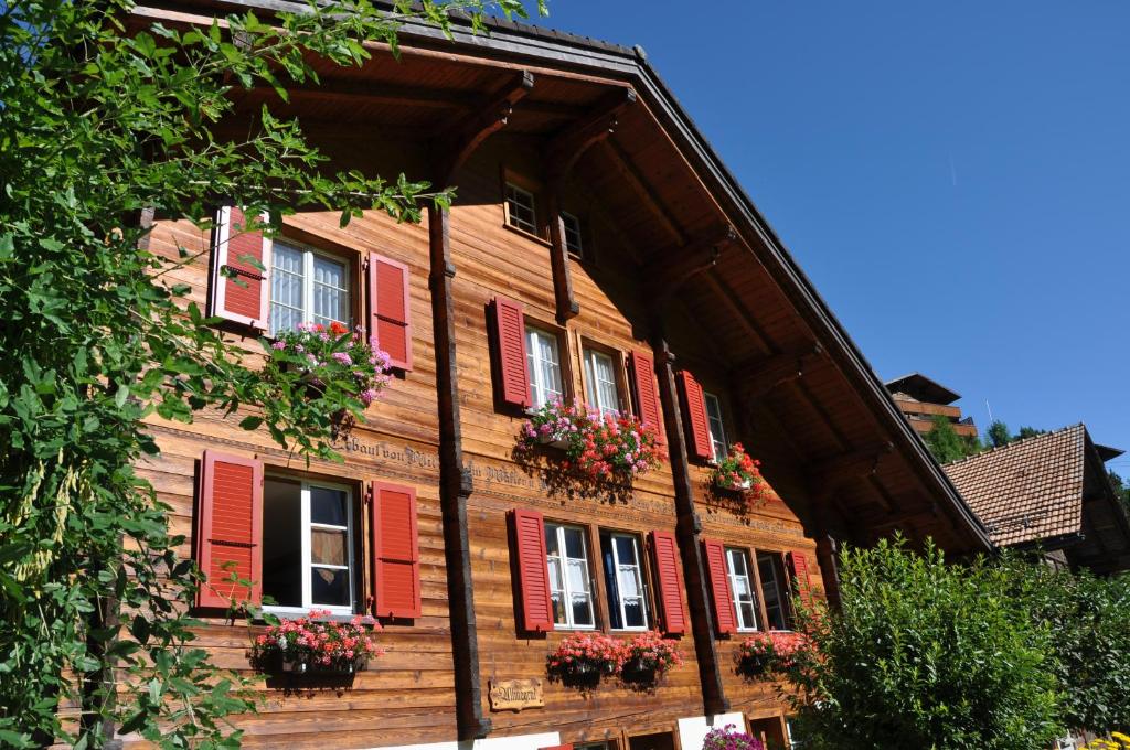 een houten huis met rode luiken en bloembakken bij Chalet Allmegrat in Adelboden