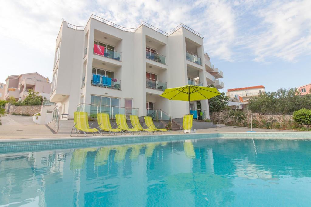 a pool with chairs and an umbrella and a building at Villa Sunset in Rogoznica