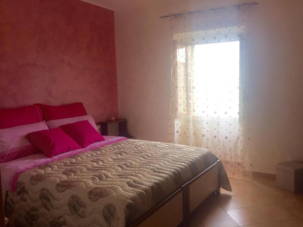 Schlafzimmer mit einem Bett mit rosa Kissen und einem Fenster in der Unterkunft A due passi in Pietrapertosa