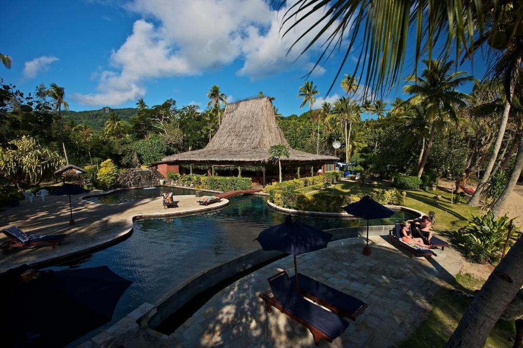 una piscina en un complejo con gente sentada bajo sombrillas en Beqa Lagoon Resort, en Beqa Island