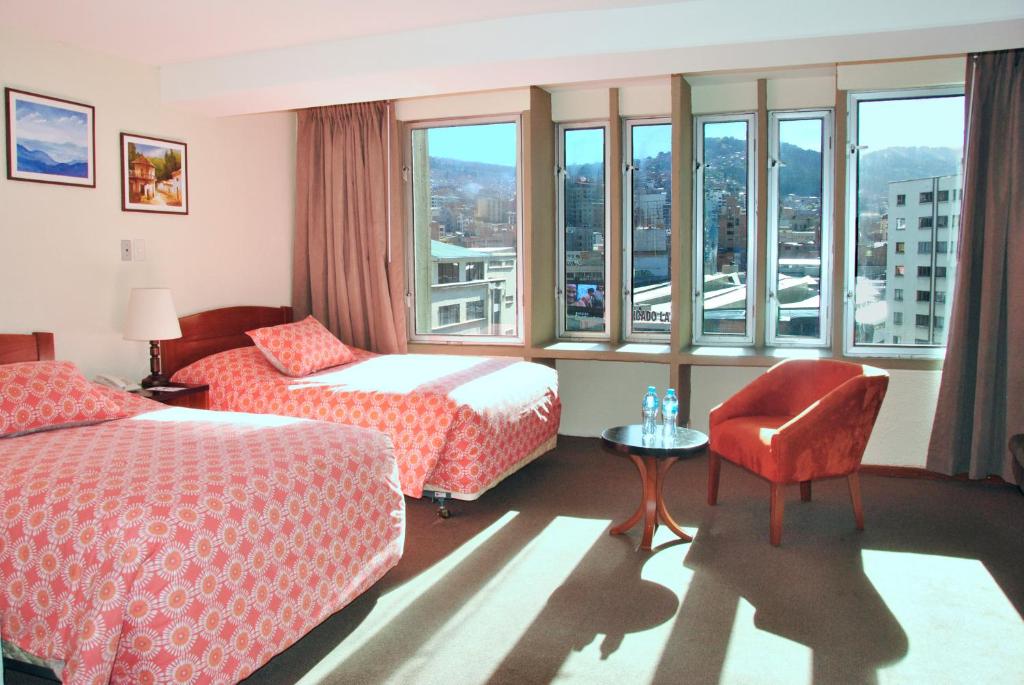 a hotel room with two beds and a chair and windows at Hotel Gloria La Paz in La Paz