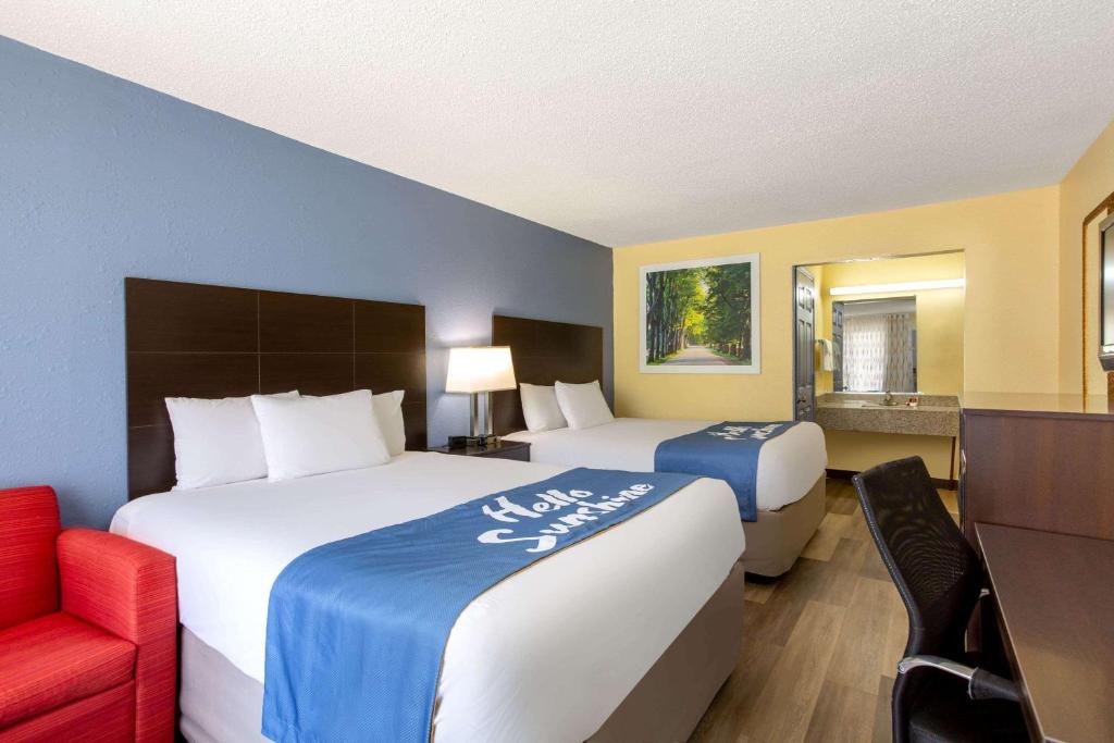 a hotel room with two beds and a red chair at Days Inn by Wyndham Greensboro Airport in Greensboro