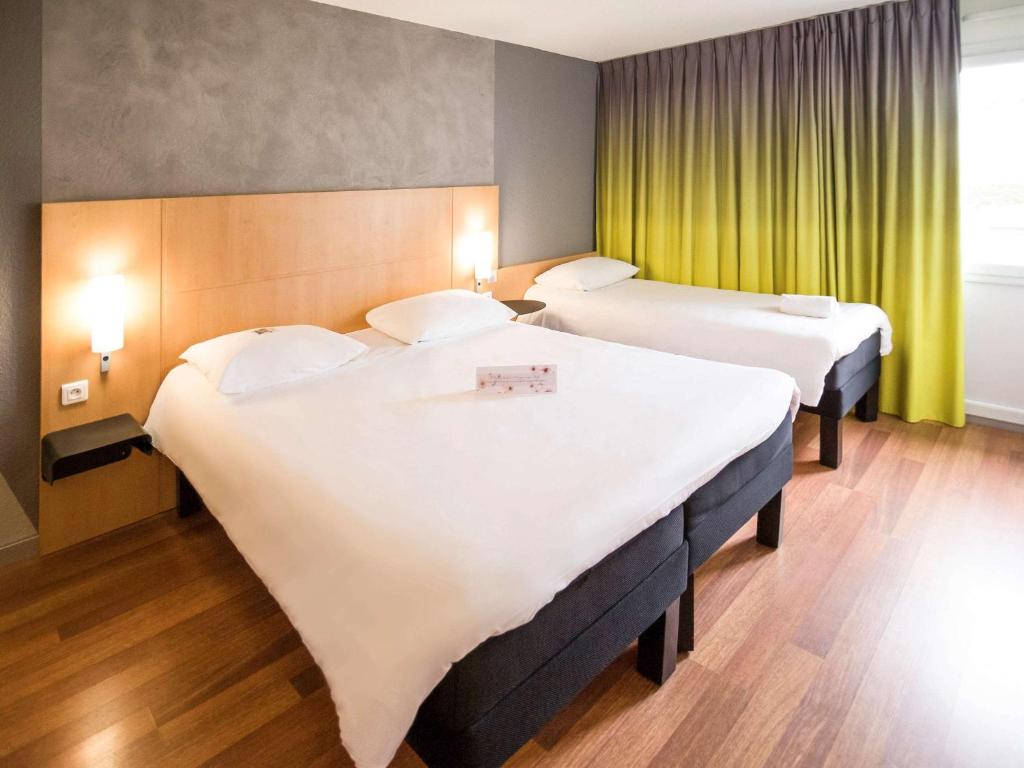a hotel room with two beds and a window at ibis Rennes Beaulieu in Cesson-Sévigné