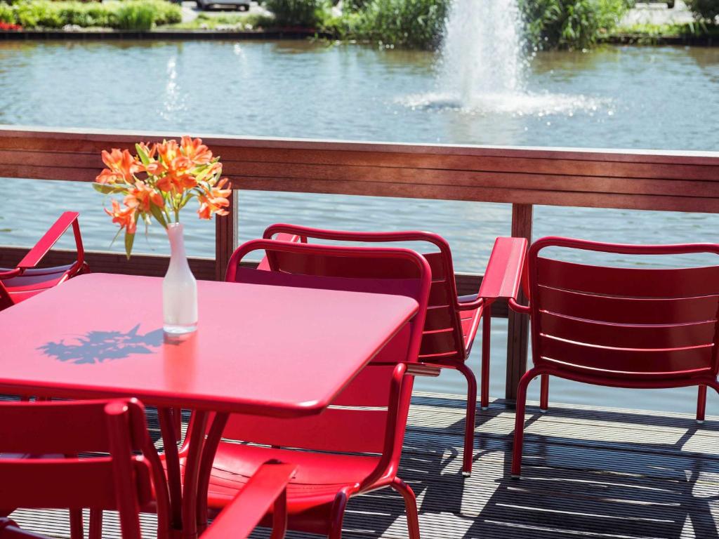 a red table and chairs with a vase of flowers on a patio at Ibis Schiphol Amsterdam Airport in Badhoevedorp