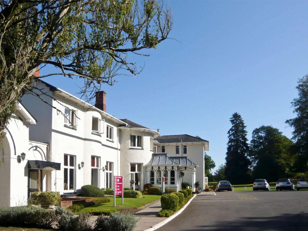 a white house with cars parked on the street at Brandon Hall Hotel & Spa Warwickshire in Brandon