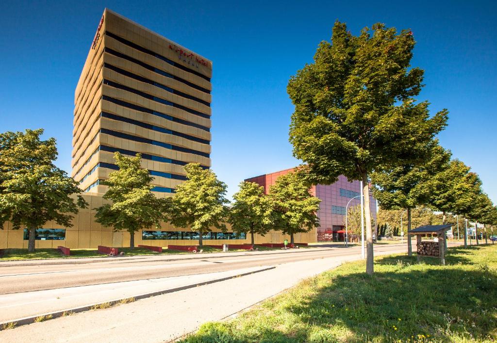 a tall building next to a street with a tree at Airport Hotel Basel - Convenient &amp; Friendly in Basel