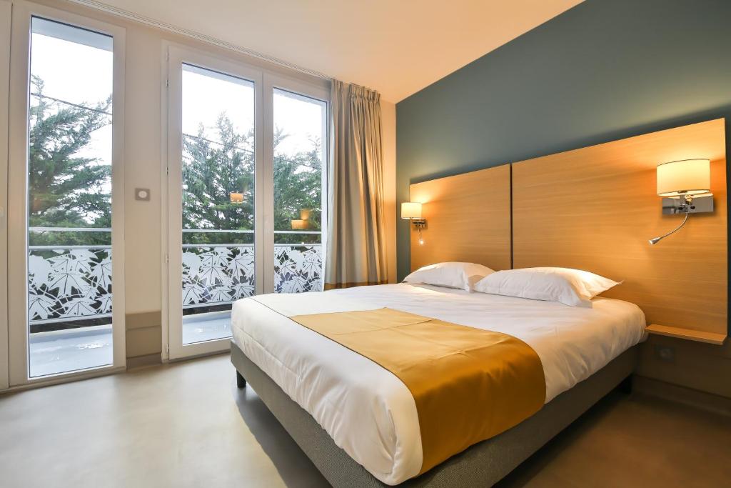 a bedroom with a large bed and two windows at Vent d'Eden Park Hôtel in Saint-Hilaire-de-Riez