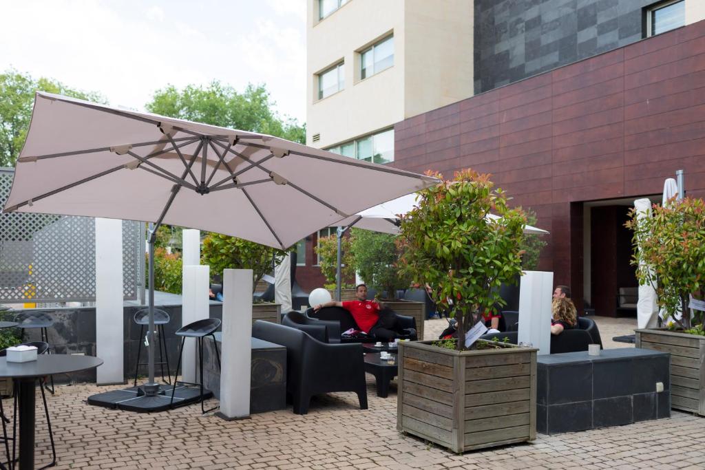 a patio with people sitting in chairs and an umbrella at PCM Forum Alcalá in Alcalá de Henares