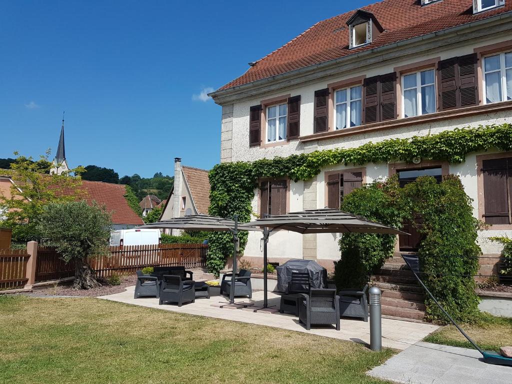 uma casa com um grupo de cadeiras e um guarda-sol em Ancien Presbytère Albert Schweitzer em Gunsbach