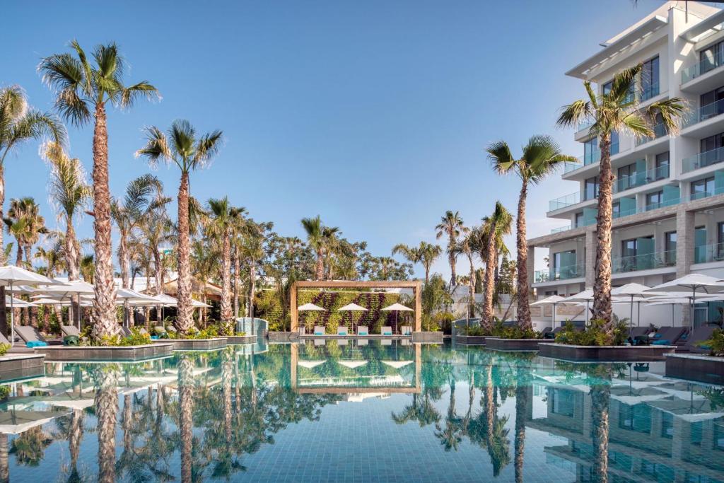 ein Resortpool mit Palmen und ein Gebäude in der Unterkunft Amavi, MadeForTwo Hotels - Paphos in Paphos City