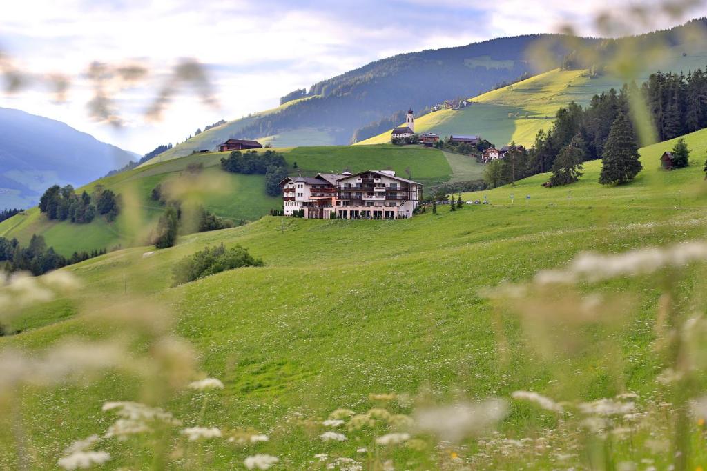 una casa en una colina en un campo verde en Bella Vista Hotel Emma, en San Vigilio Di Marebbe