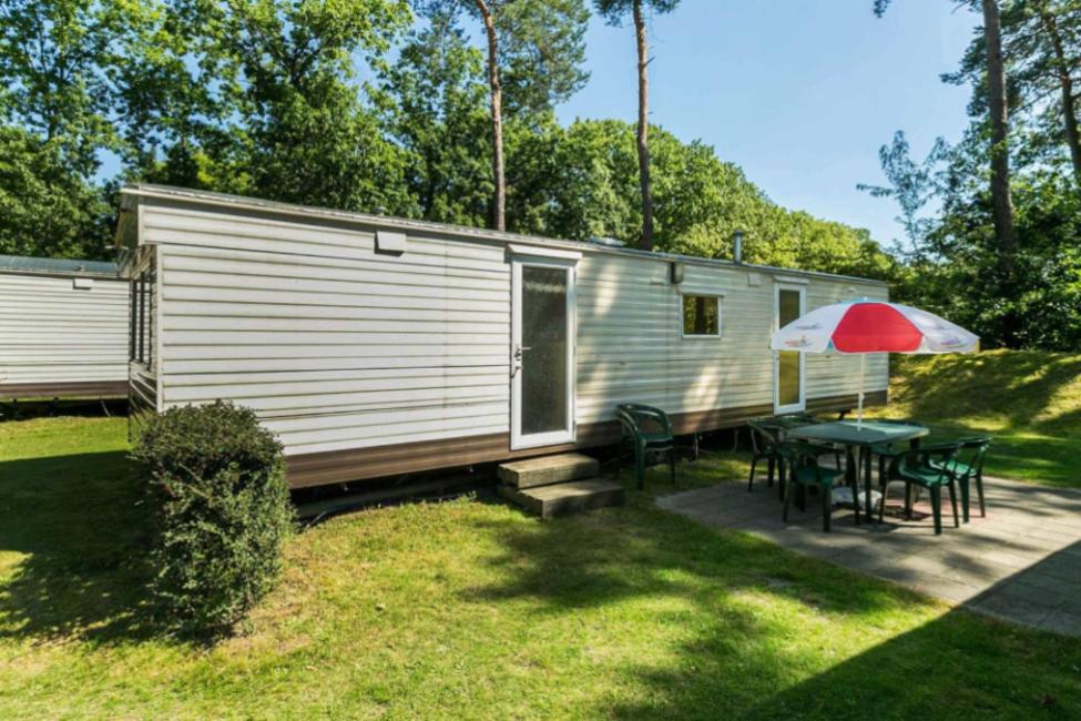 a caravan with a table and chairs and an umbrella at HH Hertenkamp Mobile Home in Aan de Wolfsberg