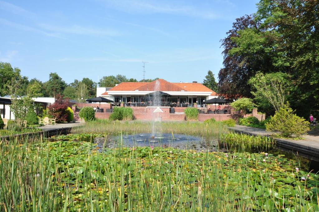 einen Teich in einem Garten mit einem Gebäude im Hintergrund in der Unterkunft Resort Bad Boekelo in Boekelo