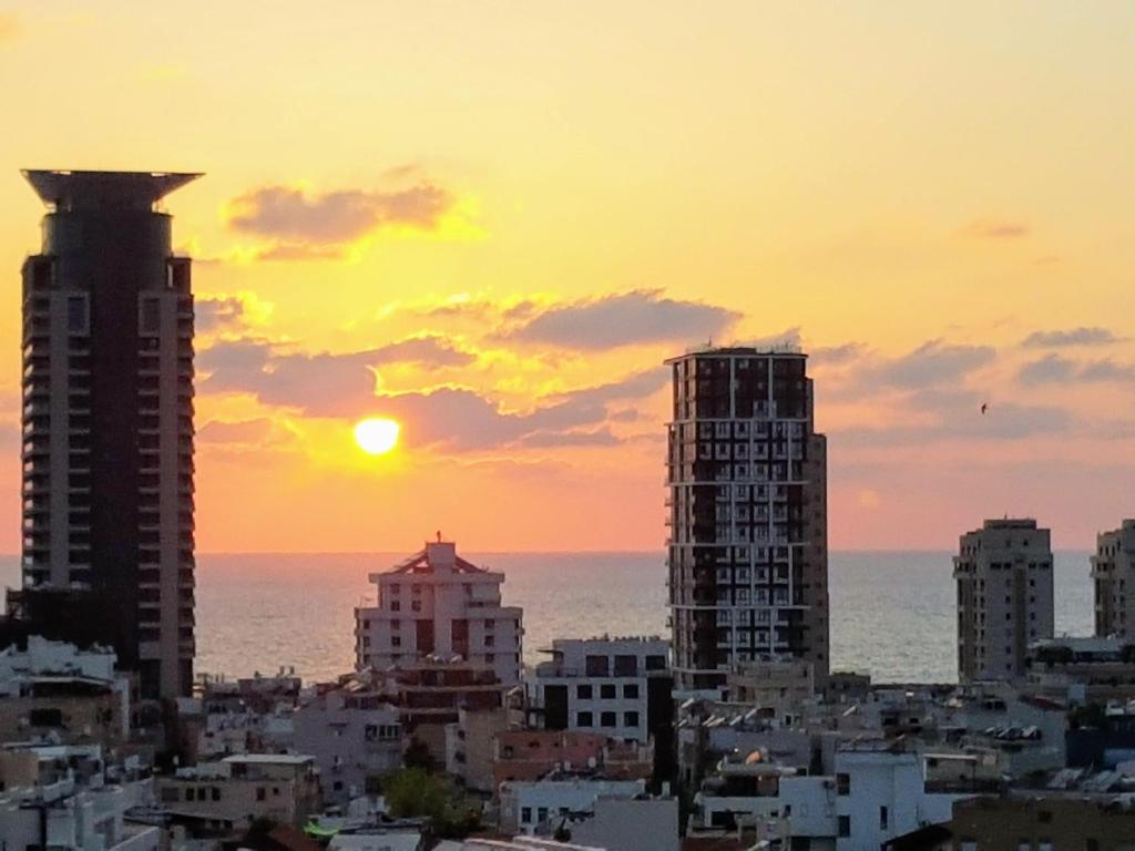 een zonsondergang boven een stad met hoge gebouwen en de oceaan bij Charming Boutique Studio - TLv Center in Tel Aviv