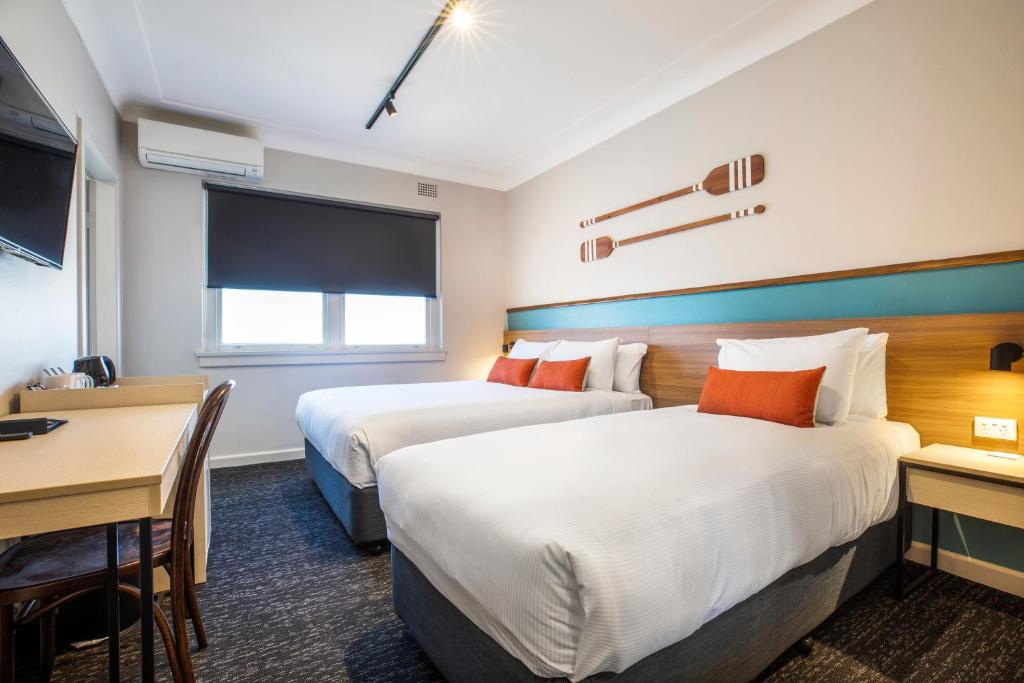 a hotel room with two beds and a table and a desk at Nightcap at Ocean Beach Hotel in Ettalong Beach