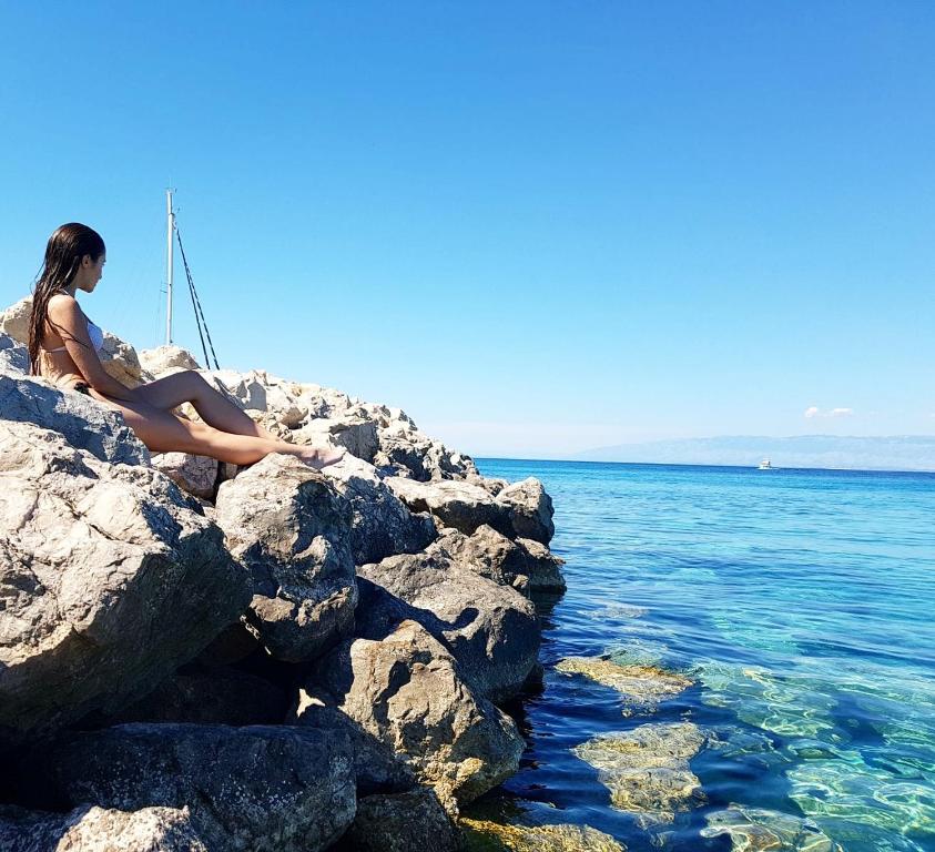 una mujer sentada en una roca junto al agua en Kuća za odmor Silba en Silba