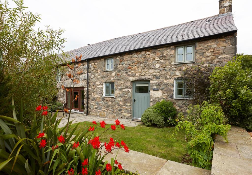 una casa de campo de piedra con flores rojas delante de ella en The Cottage Llyn Peninsula, en Nefyn