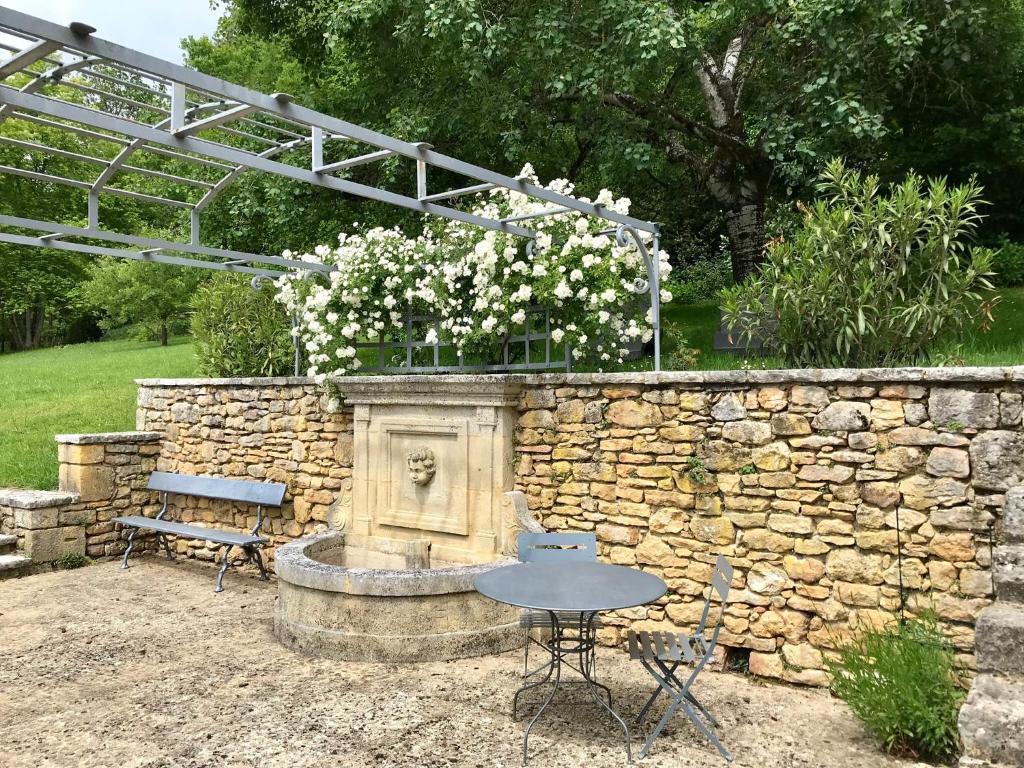 a stone wall with a fountain with a table and a bench at La Maison d&#39;Alice in Vézac