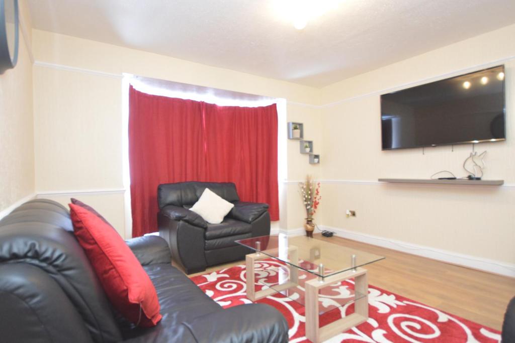 a living room with a black leather couch and a television at Four Bedroom Townhouse 12 Minutes Walk to Excel Exhibition Centre in London