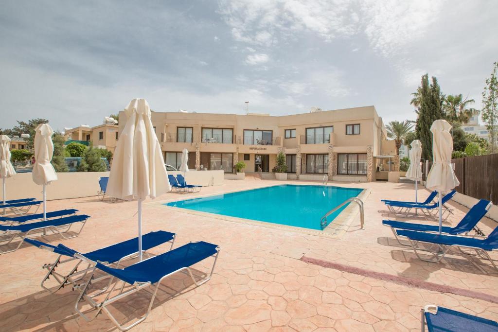 einem Pool mit Stühlen und Sonnenschirmen vor einem Gebäude in der Unterkunft Napiana Apartments in Ayia Napa