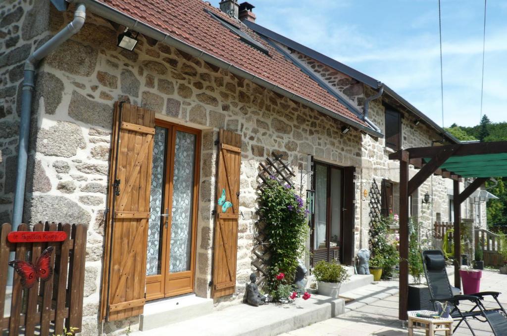 Casa de piedra con puertas de madera y valla en le Petit Papillon, en Eymoutiers