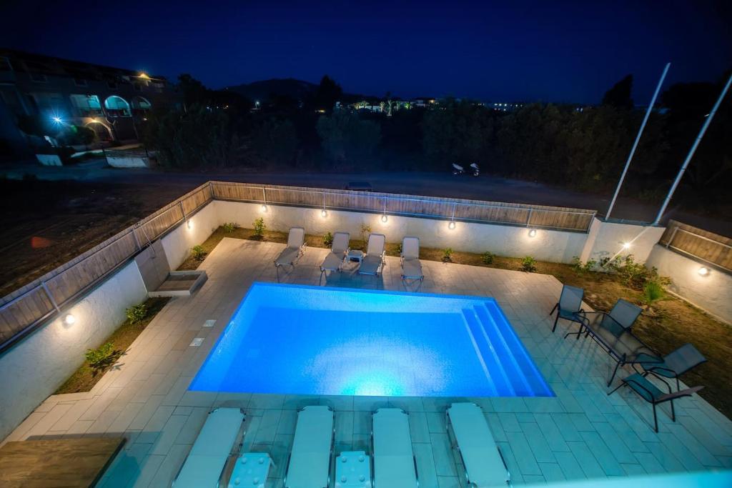 a swimming pool at night with chairs and lights at DENNIS and TANYA VILLAS in Laganas