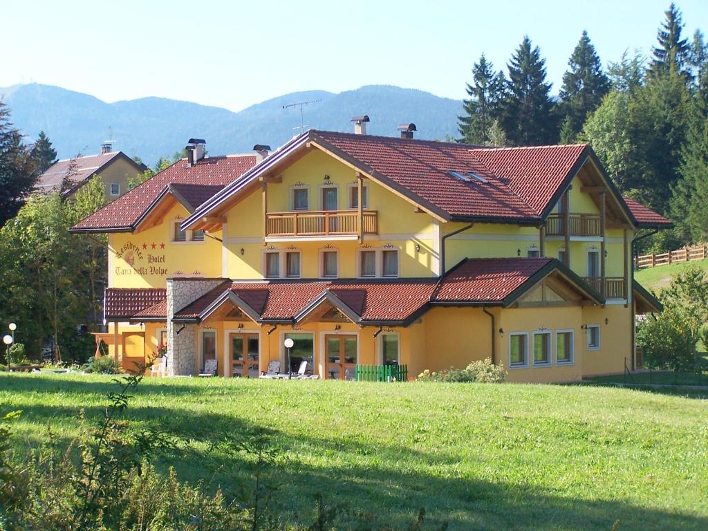 ein großes gelbes Haus mit roten Dächern auf einem grünen Feld in der Unterkunft Tana Della Volpe in Lavarone