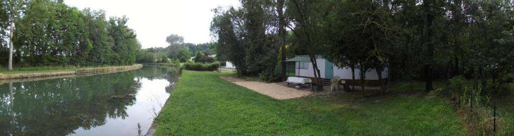 a small house next to a river with trees at Mobil-home in Ravières