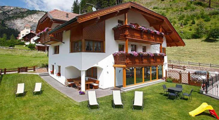 a house with a balcony on a green field at Grohmann Apartments in Selva di Val Gardena