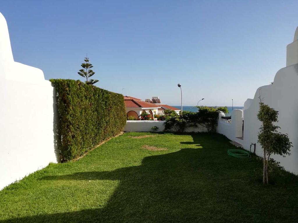 a yard with green grass next to a white wall at Two Lofts in Matalascañas