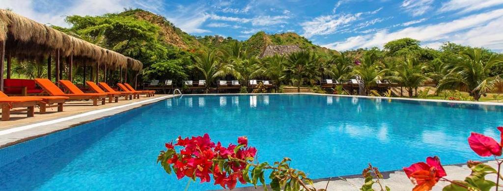 una gran piscina con sillas naranjas y flores rojas en Bungalows & Suites Punta Camarón, en Zorritos