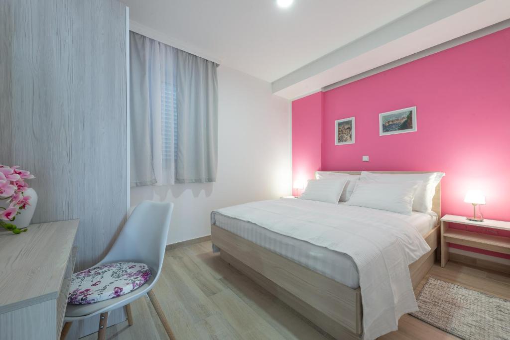 a bedroom with a pink wall with a bed and a desk at Apartments MoniDuL in Dubrovnik