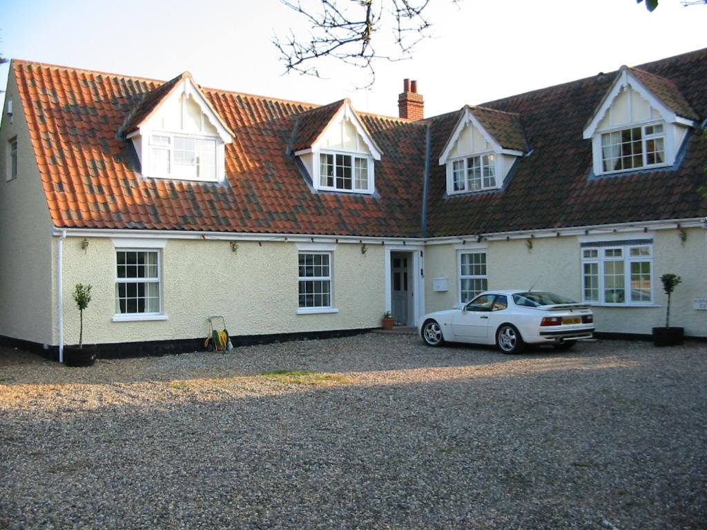 uma casa branca com um carro estacionado em frente dela em Home farm cottage Guest House em Norwich
