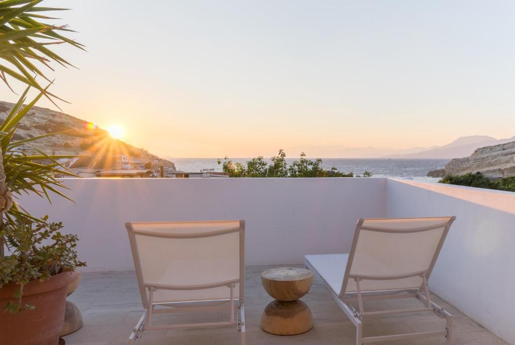 - deux chaises et une table sur un balcon avec vue sur le coucher du soleil dans l'établissement Boutique Hotel Die Zwei Brüder, à Matala