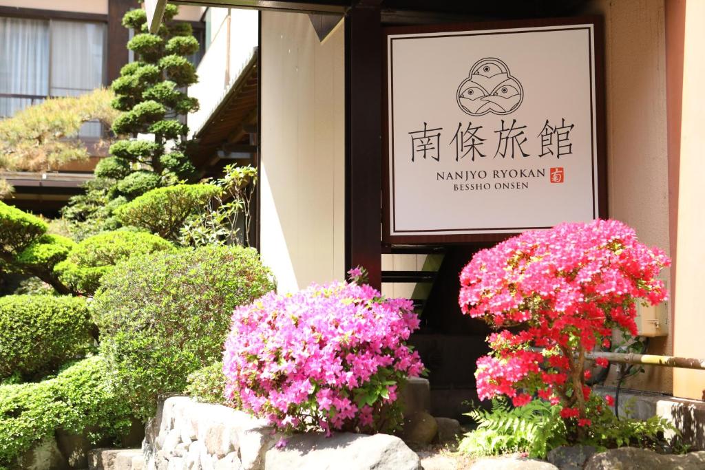 un cartel en un edificio con flores delante en Besshoonsen Nanjyo Ryokan, en Ueda