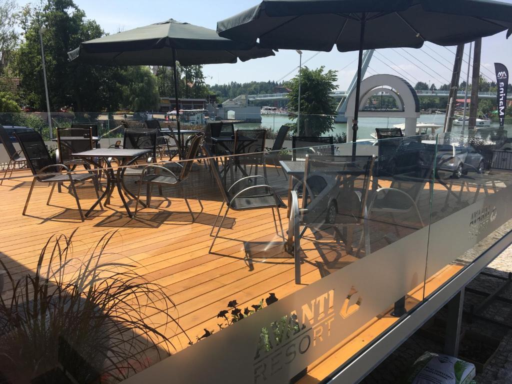 una terraza de madera con mesas, sillas y sombrillas en Avanti Resort Mikołajki , w centrum przy jeziorze i promenadzie, śniadanie i obiad lub obiadokolacja w cenie en Mikołajki