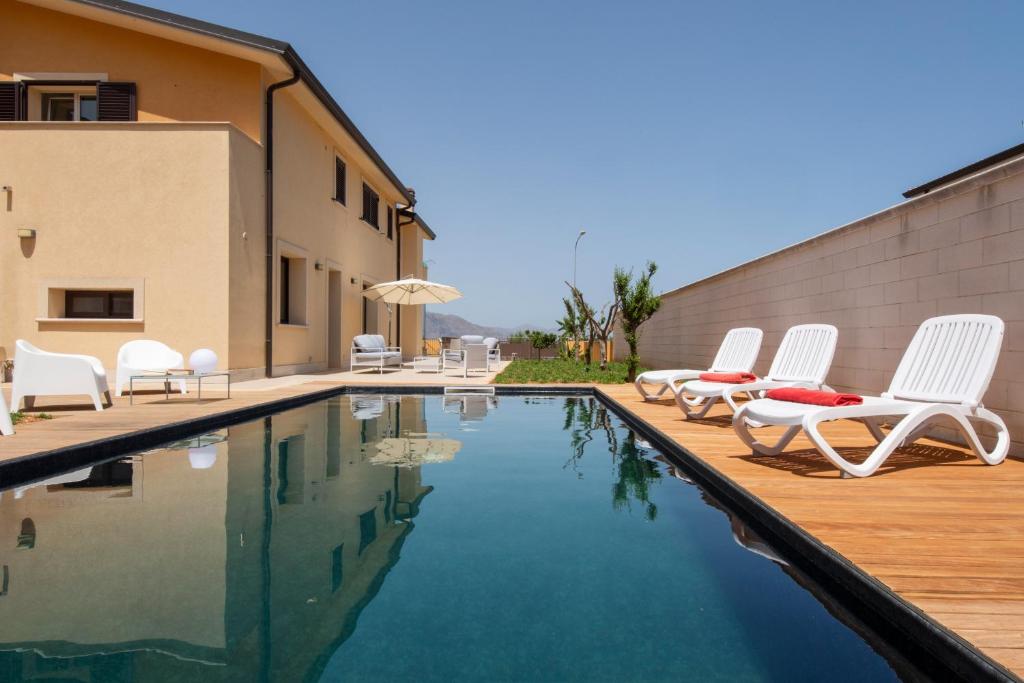 ein Pool mit weißen Stühlen und ein Gebäude in der Unterkunft Villa Uluvud by Xenia Sicily Villas in Alcamo
