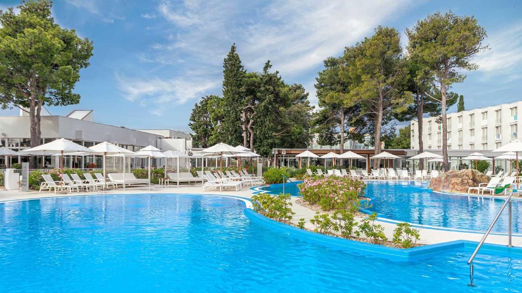 a pool at a hotel with white chairs and umbrellas at Amadria Park Family Hotel Jakov in Šibenik