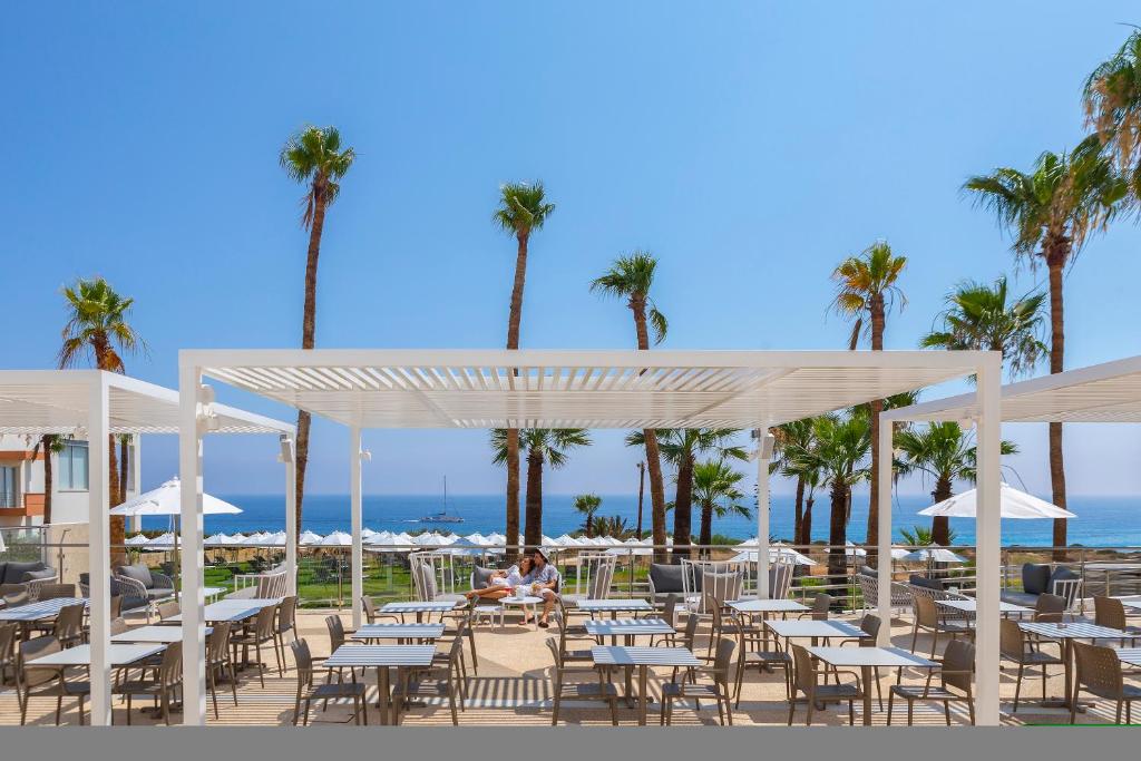 a group of tables and chairs at a beach with palm trees at Leonardo Crystal Cove Hotel & Spa – Adults only in Protaras