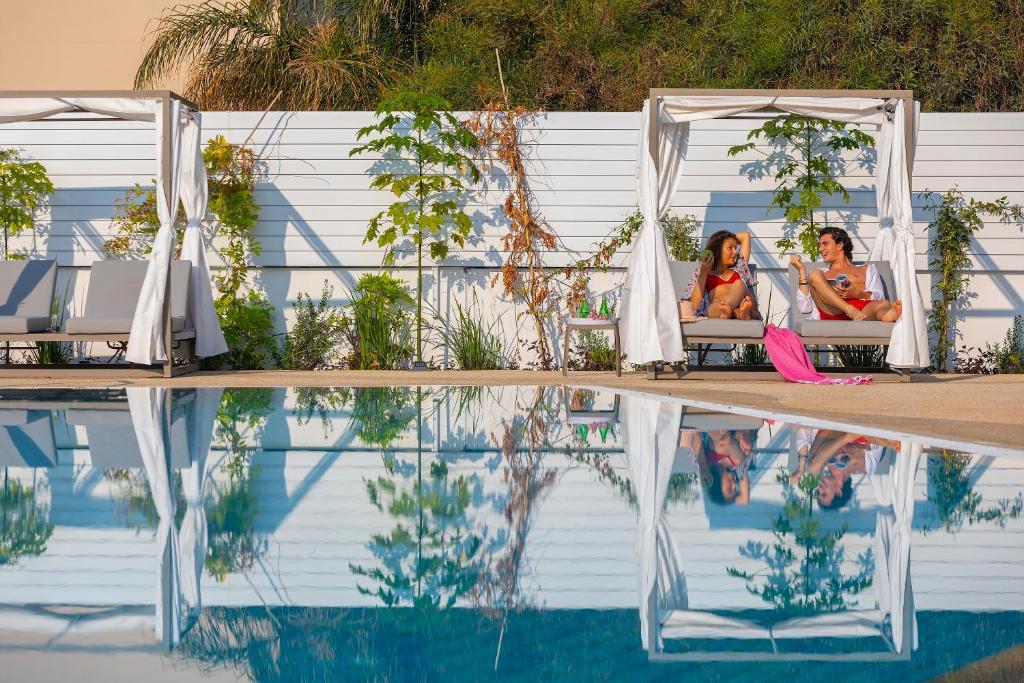 two women sitting on a bench next to a swimming pool at Leonardo Crystal Cove Hotel & Spa – Adults only in Protaras