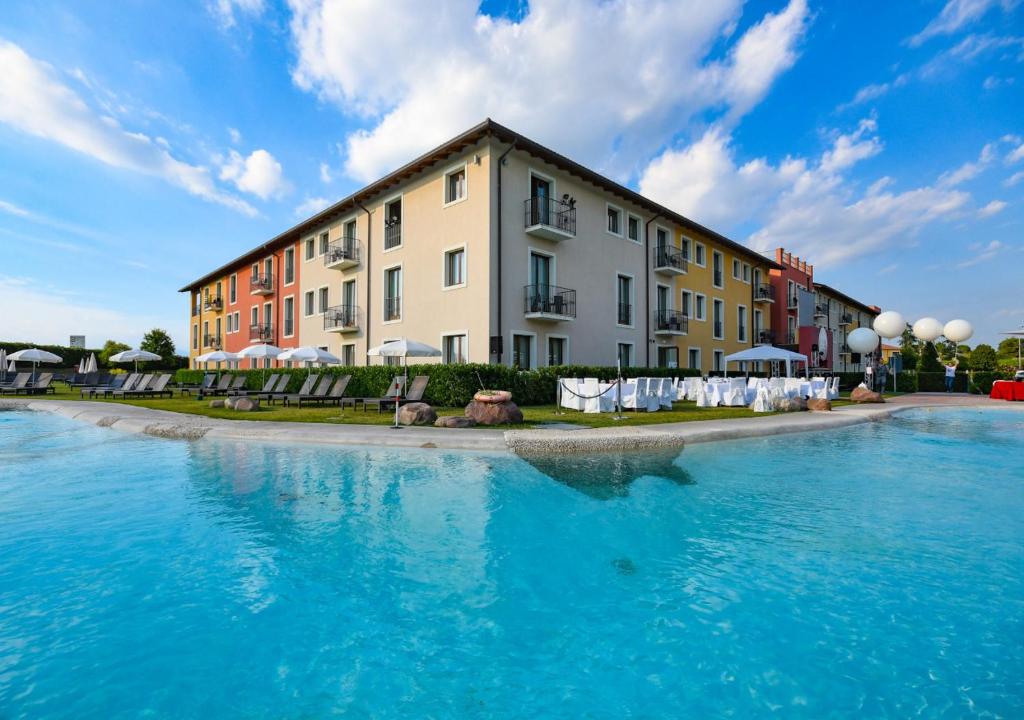 a building with blue water in front of a building at TH Lazise - Hotel Parchi Del Garda in Lazise