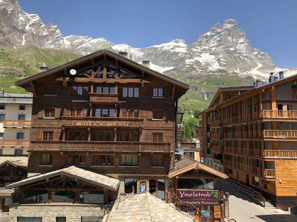 a large wooden building with mountains in the background at Hotel Punta Maquignaz in Breuil-Cervinia