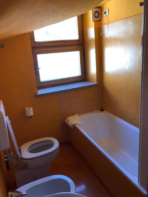 a bathroom with a toilet and a tub and a window at Hotel Punta Maquignaz in Breuil-Cervinia