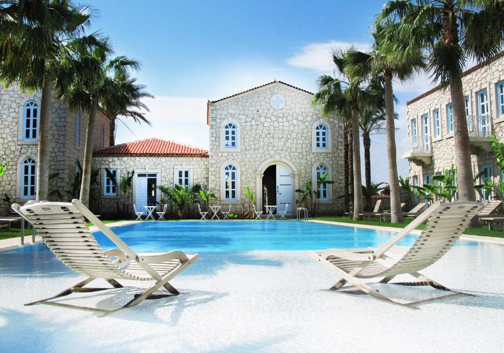 2 sillas y una piscina frente a un edificio en Manastir Alacati Hotel, en Alacati