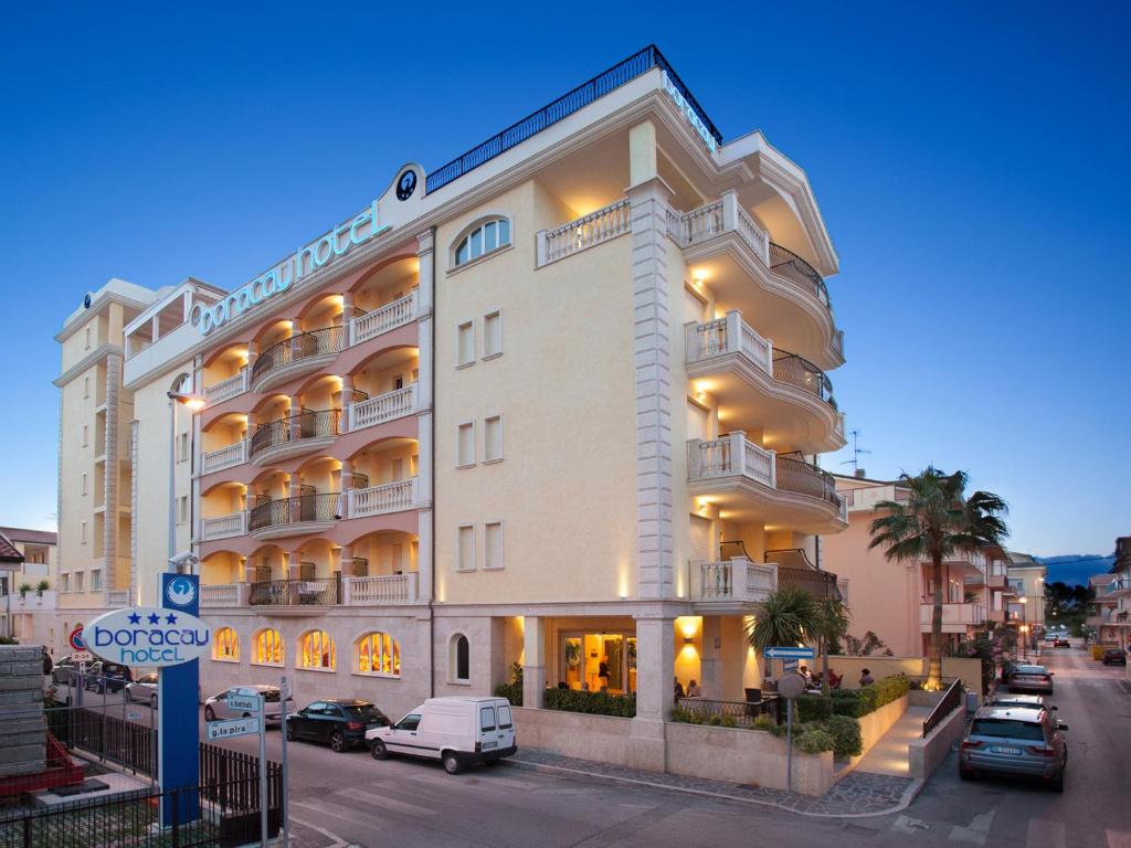 een groot wit gebouw met auto's geparkeerd voor het bij Hotel Boracay in Alba Adriatica