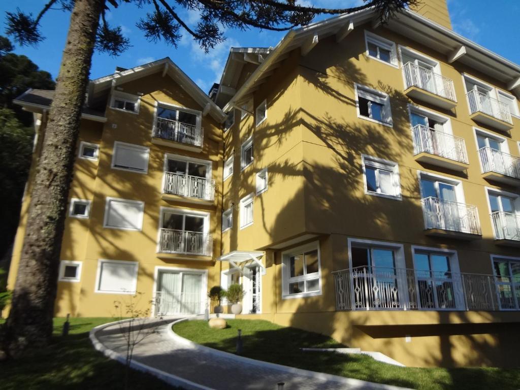 a yellow building with white windows and a tree at Apartamento 105 da Borges in Gramado