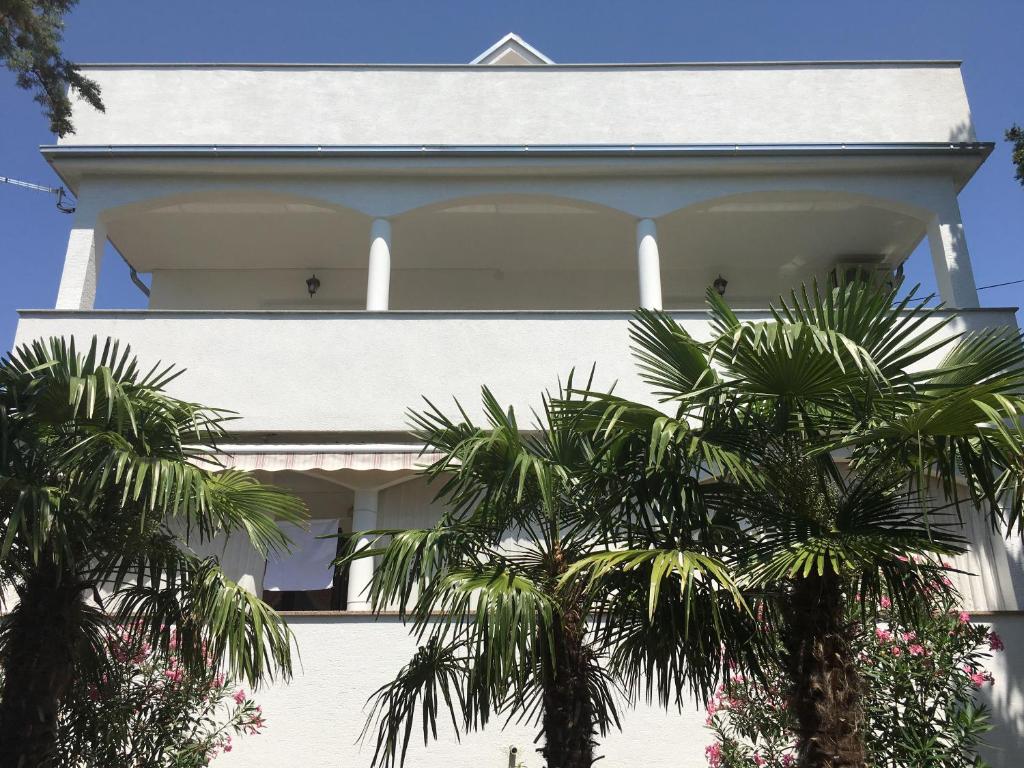 a white house with palm trees in front of it at Apartman Mirno More in Selce